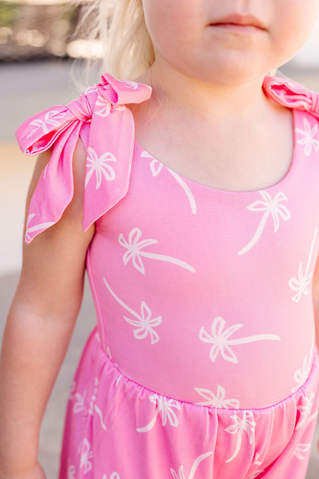 Pink romper with white floral palm tree worn by a child
