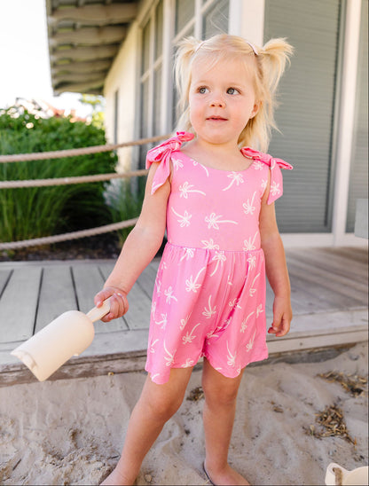 Young girl in a pink outfit with butterfly design standing on a sandy surface.