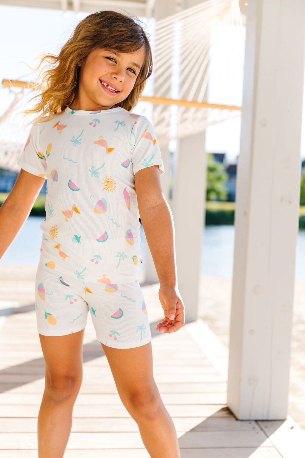 Child wearing a colorful outfit with a beachy themed pattern on a wooden deck.