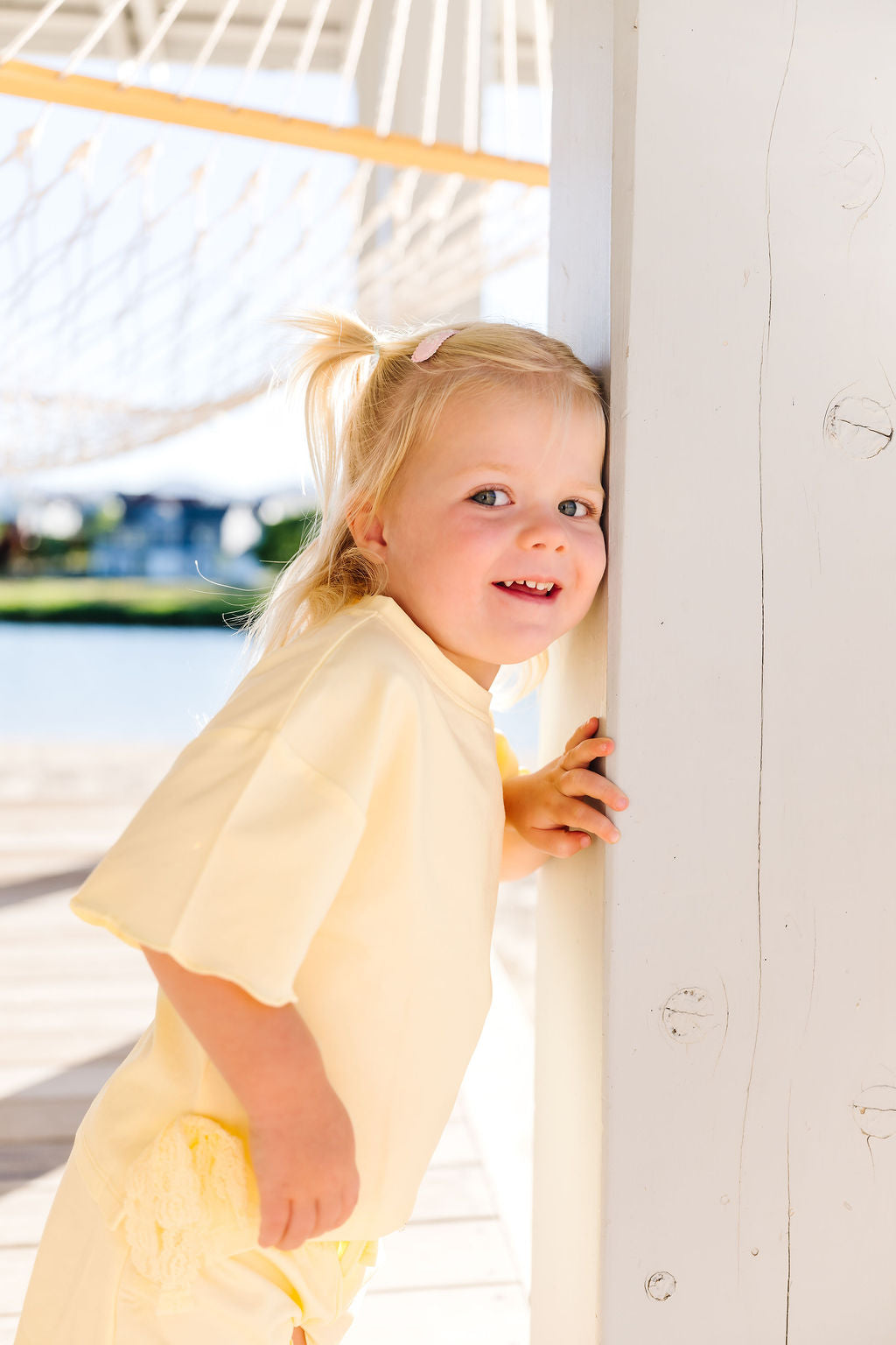 Young girl in a yellow outfit standing by a white pole with a blurred beach background
